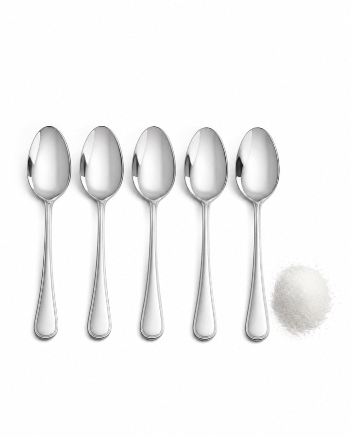 Five empty teaspoons in a row with a small pile of sugar beside them