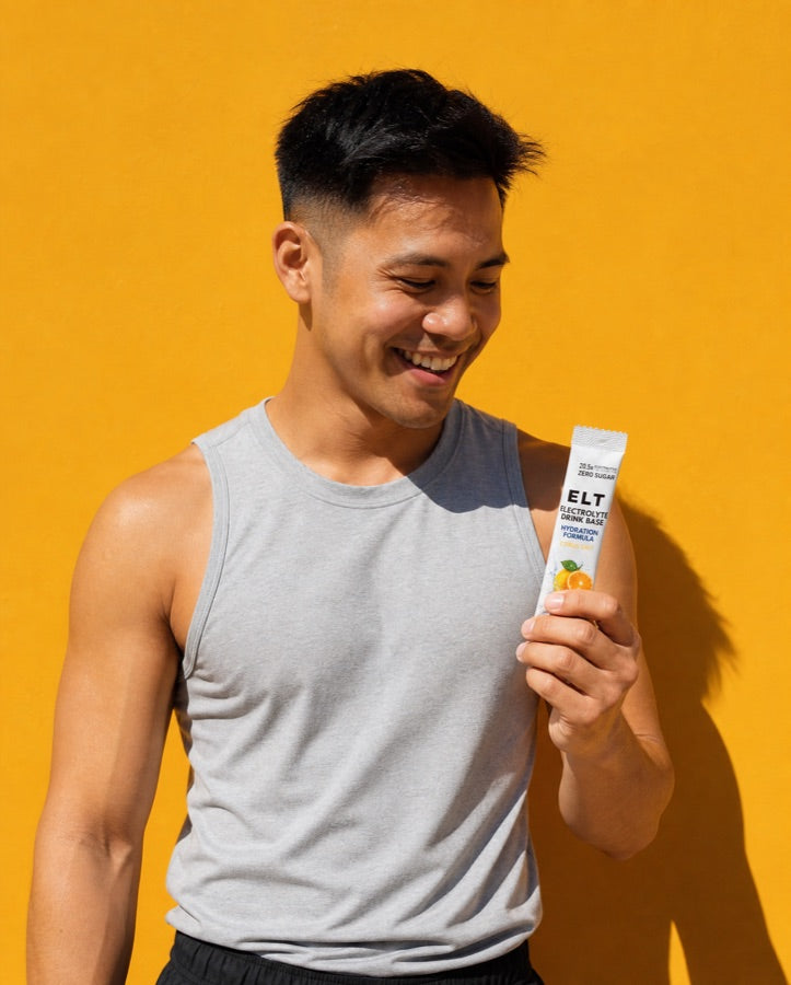 Smiling man in sportswear against a honey-yellow wall in direct sun, looking down at an ELT sachet in his hand