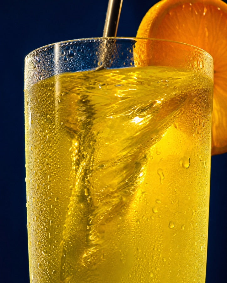 Extreme close-up of an ice-cold glass of honey-lemon ELT mid-stir with an orange wheel