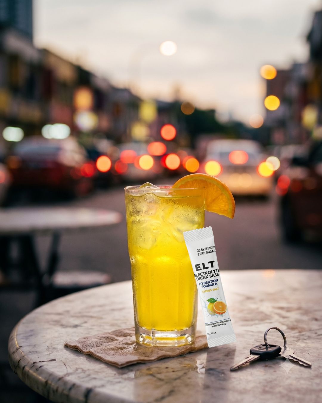 An ice-cold glass of bright lemon-yellow ELT with an orange wheel and a sachet on a marble kopitiam table, on a warm Malaysian street at dusk